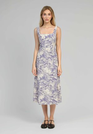 Une robe sans manches à encolure carrée en crème avec un motif floral violet. Le tissu a une texture lisse et tombe à une longueur midi.