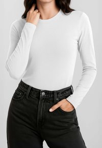 Top bianco a maniche lunghe in tessuto liscio, abbinato a jeans neri a vita alta con design classico a cinque tasche e chiusura con bottone.