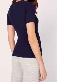Navy ribbed short-sleeve top with a fitted design, paired with light gray plaid pants. Smooth texture, simple neckline, and subtle form-fitting silhouette.