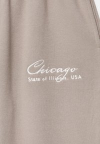 Grått tyg med en blank yta som har vit broderad text: "Chicago State of Illinois, USA" i ett kursivt teckensnitt.