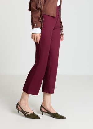 Pantaloni bordeaux corti abbinati a una giacca marrone con frange. Il modello indossa decolleté slingback verde scuro con punta a punta e tacco basso.