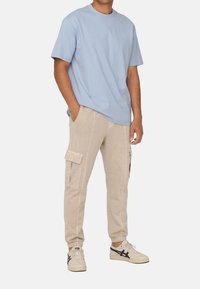 Lyseblå t-shirt med korte ærmer parret med beige cargo-sweatpants med sidelommer og kontrastsyninger. Hvide sneakers med marineblå detaljer.