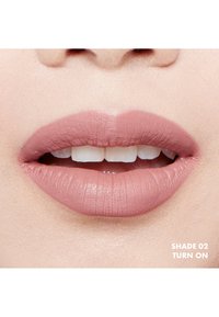Matowa pomadka w delikatnym różowym odcieniu. Usta są gładkie z wyraźnymi krawędziami, prezentując naturalny wygląd. Odcień oznaczony jako "Turn On".