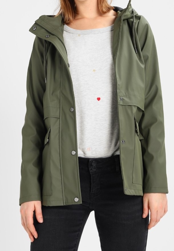 Grøn vandtæt jakke med hætte, der har trykknapper og sidelommer. Båret over en lysegrå sweater med små farvede detaljer.