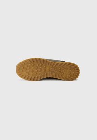 Suola di scarpa con un design in gomma testurizzata, caratterizzata da grandi tacche per la trazione, di colore beige, con una superficie piatta e una leggera curvatura.