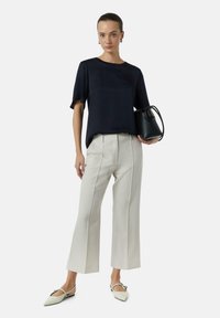Marinebluse mit kurzen Ärmeln, cremefarbene weit geschnittene Hose und spitze Ballerinas. Schwarze Handtasche mit kurzem Henkel, minimalistisches Design.