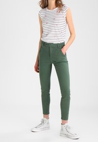 Zielone bawełniane spodnie slim fit z wysokim stanem i dwoma przednimi kieszeniami, zestawione z krótkim rękawem w paski oraz białymi trampkami.