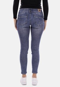 Jeans skinny in denim blu medio, con vita media, due tasche posteriori con cuciture decorative, completati da sneakers bianche.