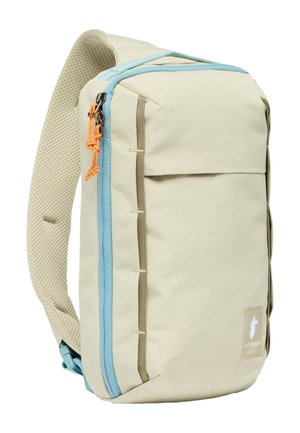 Beiger Rucksack mit hellblauem Reißverschluss, grünen Akzenten und einem strukturierten Schultergurt. Verfügt über eine Fronttasche und verstärkte Nähte.