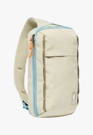 Beiger Rucksack mit hellblauem Reißverschluss, grünen Akzenten und einem strukturierten Schultergurt. Verfügt über eine Fronttasche und verstärkte Nähte.