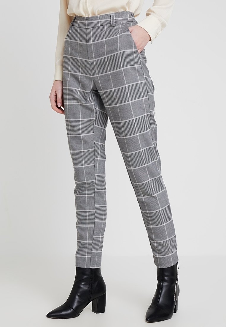 Šedé kostkované kalhoty s upraveným střihem, vybavené vysokým pasem, bočními kapsami a jemnou texturou, spárované s černými kotníkovými botami.