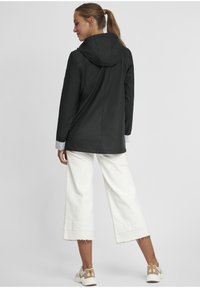 Black waterproof jacket with a hood, featuring a simple design and striped cuffs. Worn with white wide-leg pants and beige shoes.