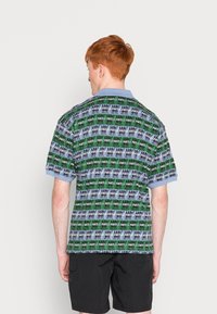 Kortermet polo-skjorte med et flerfarget mønster av svart, grønn og blå. Har en lys blå krage og en avslappet passform.