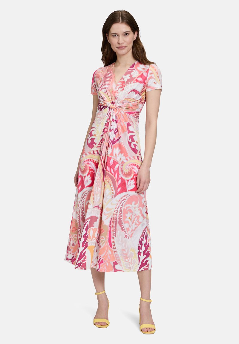 Robe florale rose avec un nœud à l'avant, manches courtes et longueur midi fluide, présentant un motif paisley multicolore et une texture de tissu lisse.