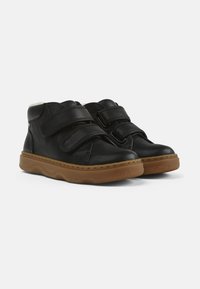 Zapatos negros de cuero de caña alta con dos correas de Velcro, un suave forro blanco y una suela de goma marrón con un patrón ondulado.