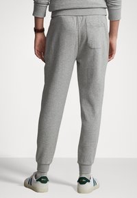 Grå mjukisbyxor i ett mjukt material med en avsmalnande design. Har en elastisk midja och en bakficka. Ett par vita sneakers syns.