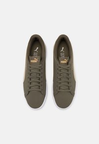 Ett par olivgröna Puma-sneakers med bruna detaljer, snörda, sedd uppifrån mot en vit bakgrund.