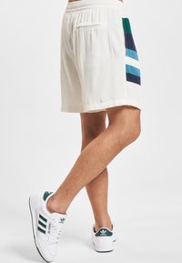 Kermanväriset shortsit, joissa on joustava vyötärönauha ja monivärinen raidallinen kuvio vihreän, laivastonsinisen ja sinisen sävyissä sivussa.