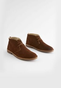 Ruske mokka nilkkurit, joissa on sileä pinta, pyöreä varvastyyny, etulenkki ja vaaleanbeige fleece-vuori. Ompeleet korostavat pohjaa.