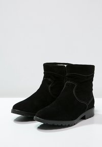 Botas de tobillo de ante negro con puntera redondeada, costuras contrastantes en blanco, un suave forro interior y una suela de goma texturizada.