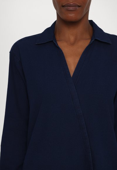 Mörkblå skjorta med krage har långa ärmar och en vrapdesign i ett texturerat tyg. Rena sömmar och en snygg finish är anmärkningsvärda detaljer.