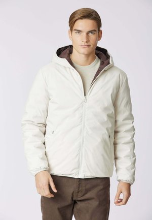 Giacca leggera di colore crema con zip frontale e cappuccio, dotata di polsini elastici e fodera marrone. Texture liscia, design casual.