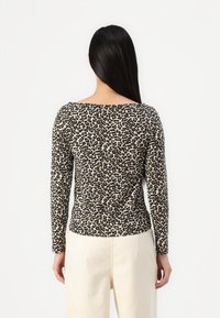 Top cu imprimeu leopardo, cu mâneci lungi și decolteu larg, realizat dintr-un material moale, având o formă ajustată și un tiv negru contrastant la gât.