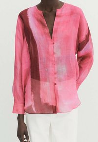 Blouse légère et transparente de couleur rose avec des motifs abstraits en coups de pinceau rouges et bleus, décolleté en V et fermeture par bouton ; manches longues avec coupe ample.