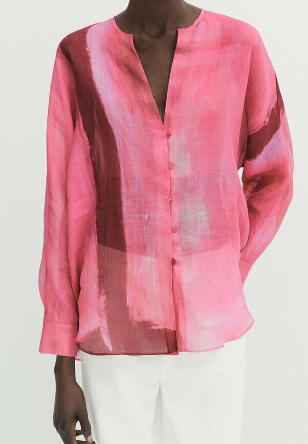Blouse légère et transparente de couleur rose avec des motifs abstraits en coups de pinceau rouges et bleus, décolleté en V et fermeture par bouton ; manches longues avec coupe ample.