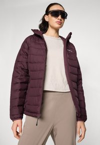 Maroon puffer jacket with a zippered front and hood, featuring quilted design and elastic cuffs. Paired with a light-patterned top.