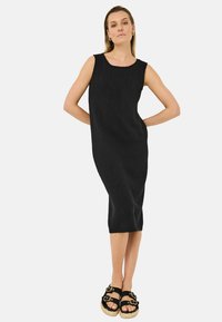 Svart, ärmlös klänning med rundad halsringning, figursydd silhuett, mjukt material och knälängd. Bärs med svarta och bruna sandaler med remmar.