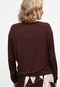 Bruine lange mouwen top met een relaxte pasvorm en raglanmouwen, gemaakt van zachte stof. De achterkant heeft een gladde textuur met een afgeronde halslijn.