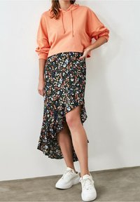 Korálový krátký svetr spárovaný s černou květinovou středně dlouhou sukní se zdobeným lemem. K outfitu se hodí bílé tenisky.