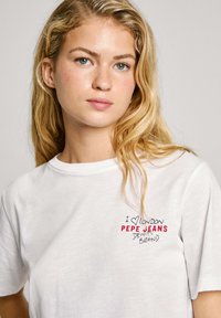 Bílá bavlněná tričko s malým vyšitým designem "I ❤️ London" v modré a červené barvě a nápisem "PEPE JEANS DENIM BRAND" v černé.