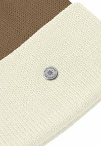 Tessuto intrecciato marrone e crema con superficie strutturata, caratterizzato da un bottone rotondo in metallo argentato con logo in rilievo.