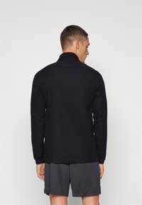 Suéter negro de manga larga con cuello alto, hecho de una tela suave, presenta un dobladillo recto y un corte relajado, combinado con pantalones cortos grises.