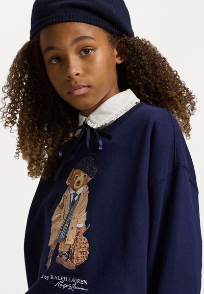 Sudadera navy con textura tejida, que presenta un gráfico de un oso con abrigo y sombrero. Cuello blanco con bordes ondulados y detalle de lazo.