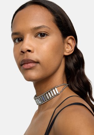 Naszyjnik choker z prostokątnymi akcentami w metalicznym srebrnym kolorze, z koralikowym łańcuchem. Charakteryzuje się gładką teksturą i warstwowym wzornictwem.