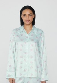 Satin-Pyjama-Oberteil in Mintgrün mit floralem Muster. Verfügt über einen spitzen Kragen, lange Ärmel und eine durchgehende Knopfleiste mit hellrosa Blumen.
