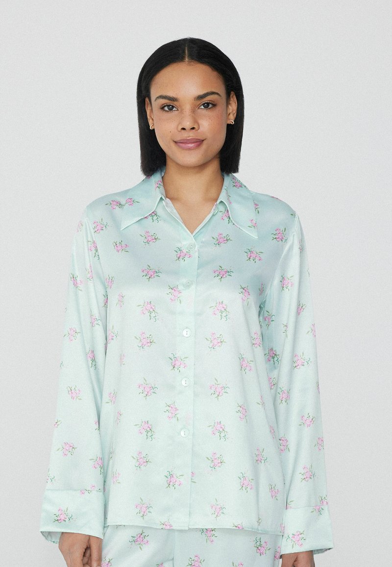 Satin-Pyjama-Oberteil in Mintgrün mit floralem Muster. Verfügt über einen spitzen Kragen, lange Ärmel und eine durchgehende Knopfleiste mit hellrosa Blumen.