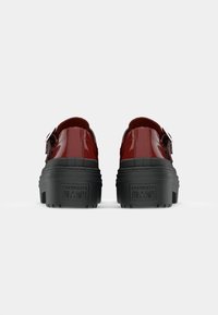 Scarpe in pelle patinata rossa con suola in gomma nera spessa, dotate di una fibbia laterale e una superficie texture. Logo sul tacco.