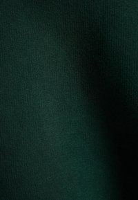 Tmavě zelená žebrovaná tkanina s hladkou texturou, zobrazující jemné vertikální čáry. Bez viditelných vzorů nebo dalších detailů.