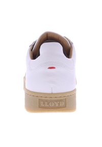 Sneaker bianca in pelle con suola in gomma texturizzata color marrone chiaro, logo "LLOYD" sul retro e un piccolo dettaglio rosso vicino alla parte superiore. Design pulito e minimalista.