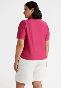 Top fucsia a maniche corte con una texture liscia, scollo rotondo e vestibilità comoda, abbinato a pantaloni corti bianchi fino al ginocchio.