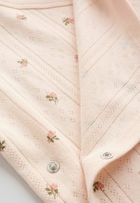 Mjukt rosa stickat tyg med små blommönster och två silverfärgade tryckknappar delvis fastknäppta.