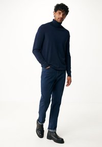 Navyblauer Rollkragenpullover, weicher Stoff, lockere Passform, kombiniert mit dunklen Jeans und schwarzen Stiefeletten mit dicker Sohle.