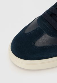 Navy suede and leather sneaker with a rounded toe, textured fabric accents, and elasticated laces. Cream rubber sole and stitching details.