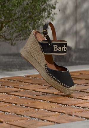 Espadrille compensée noire avec tige en toile, semelle en jute et caoutchouc, dotée d'une bride de cheville en cuir marron avec bande à logo embossée.