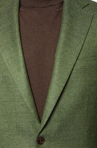 Zielona tkana marynarka z klapami, brązowy golf pod spodem, z brązowym guzikiem i fakturowanym materiałem.