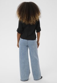 Schwarze Denimjacke mit aufgerollten Ärmeln, kombiniert mit hellblauen Schlagjeans. Der Stoff ist glatt, mit sichtbaren Nähten und ohne Muster.